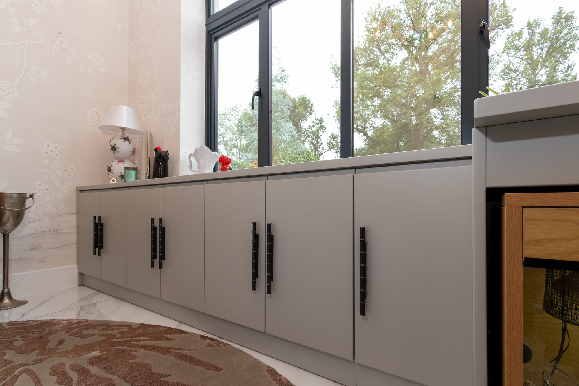 Run of grey cabinets under a window with black bamboo-form handles