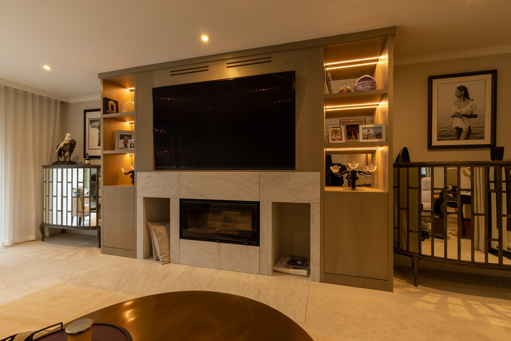 Lit display alcoves in oak flanking a wall-mounted screen and fire surround