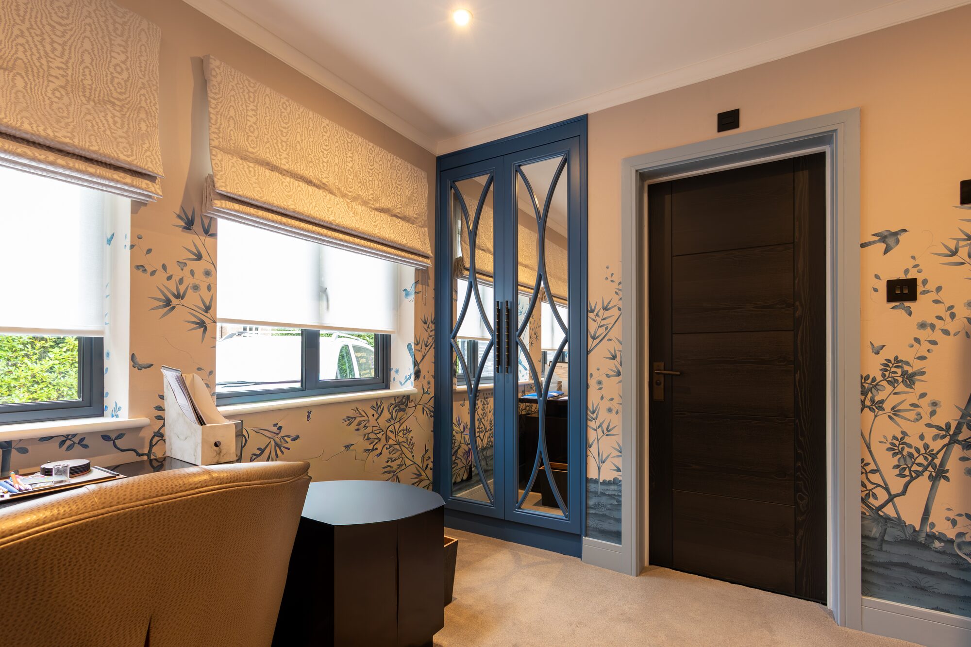 Blue lacquered cabinets with mirrored doors in a study, papered wall behind